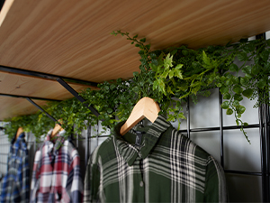 A close up shot of a shirt on a wooden hanger and some greenery hanging from wire grid